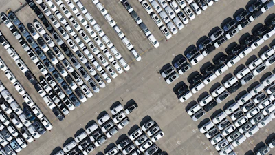 Aerial view of a large parking lot with hundreds of white, gray, and black vehicles arranged in organized rows