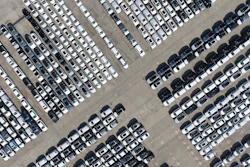 Aerial view of a large parking lot with hundreds of white, gray, and black vehicles arranged in organized rows