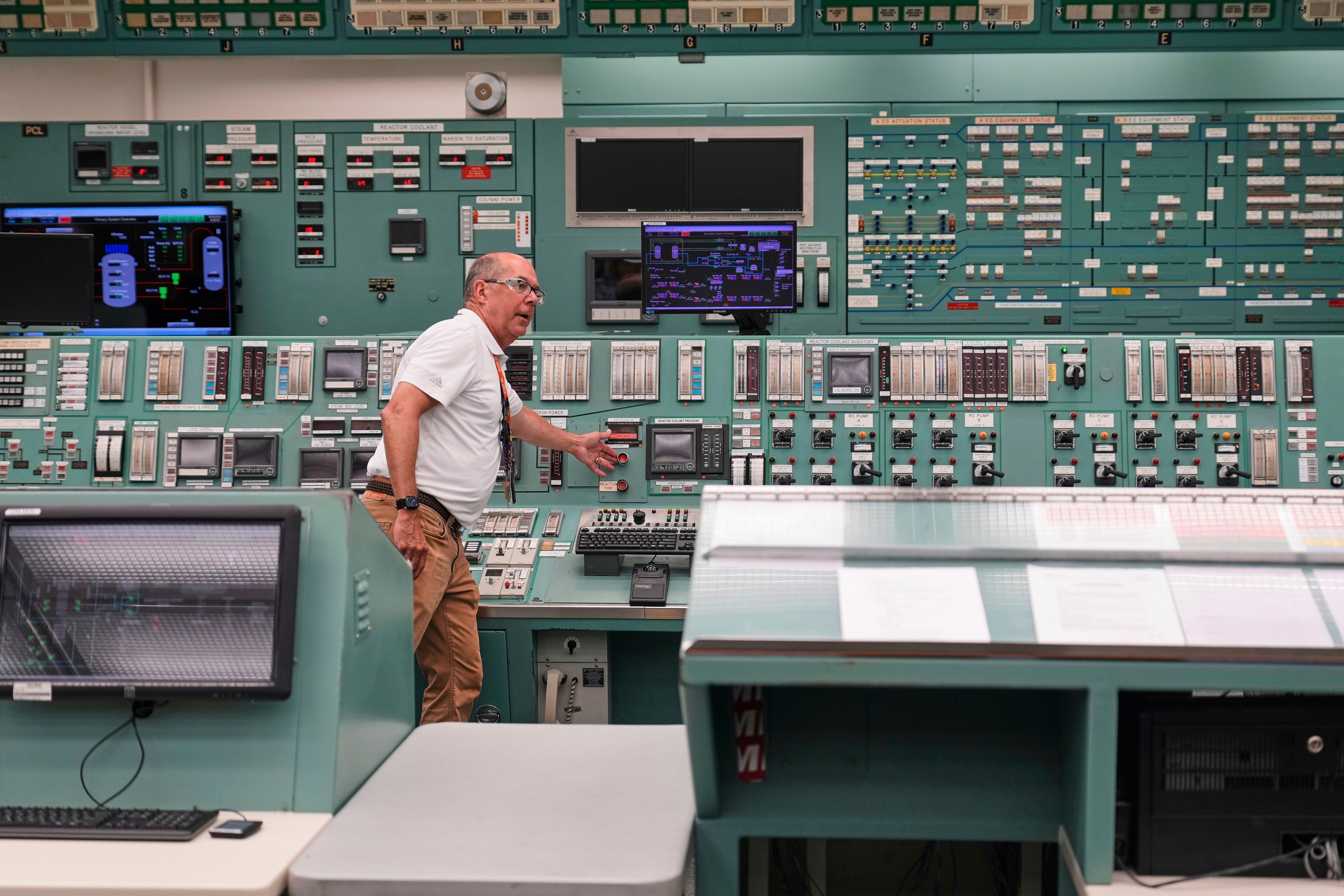 Technician operating control room with extensive monitoring equipment and instrument panels
