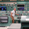 Technician operating control room with extensive monitoring equipment and instrument panels