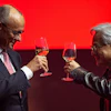 Two professionals toasting with glasses of whiskey against a red background during a formal event
