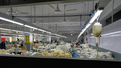 Industrial textile factory floor with workers processing fabrics at production stations under bright overhead lighting