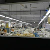 Industrial textile factory floor with workers processing fabrics at production stations under bright overhead lighting