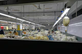 Industrial textile factory floor with workers processing fabrics at production stations under bright overhead lighting