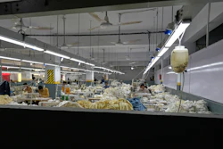 Industrial textile factory floor with workers processing fabrics at production stations under bright overhead lighting