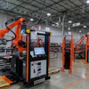 Industrial robotic welding facility with orange automation equipment and American flag in warehouse setting