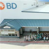 Large group of BD company employees standing together outside a modern industrial facility with white and teal metal roofing.