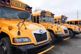 Row of yellow school buses parked in a line with bare trees in background