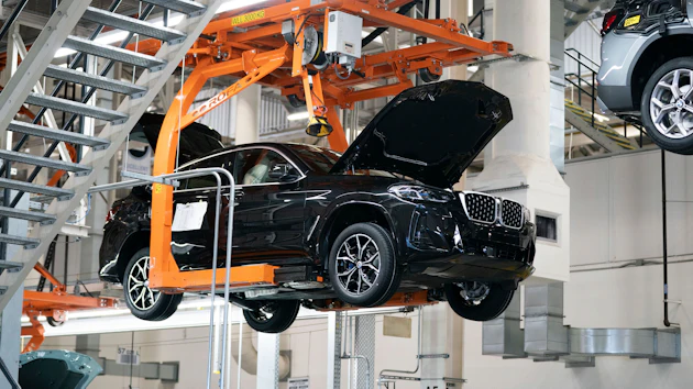 Black SUV suspended by orange mechanical lift in automotive manufacturing facility