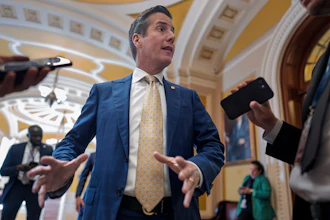 Man in blue suit and gold tie speaking to media in ornate government building corridor