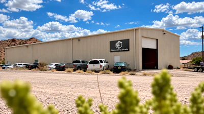 Surveying & Scale industrial warehouse building with metal siding and parked vehicles in desert landscape