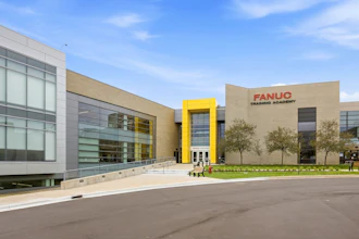 Modern FANUC Training Academy building with glass and tan facade, featuring yellow accent entrance and landscaping
