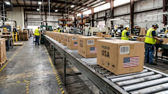 Workers in safety vests process cardboard boxes marked 'Made in USA' on a warehouse conveyor belt system.