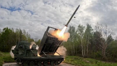 Military MLRS launcher firing a long-range missile in a forest clearing with smoke and flames visible