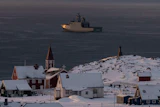 Arctic coastal settlement with red church, snow-covered buildings, and icebreaker ship in Greenlandic waters