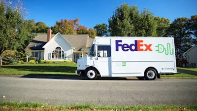 FedEx delivery truck parked on residential street in front of white house with autumn trees