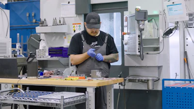 Machinist in blue gloves working at a HAAS CNC machine in an industrial manufacturing facility.