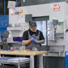 Machinist in blue gloves working at a HAAS CNC machine in an industrial manufacturing facility.
