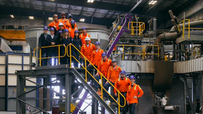 Industrial facility tour with group in orange safety uniforms on yellow metal stairs and platforms