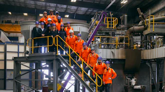 Industrial facility tour with group in orange safety uniforms on yellow metal stairs and platforms