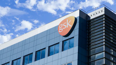 GSK corporate headquarters building with orange logo sign against blue sky and clouds
