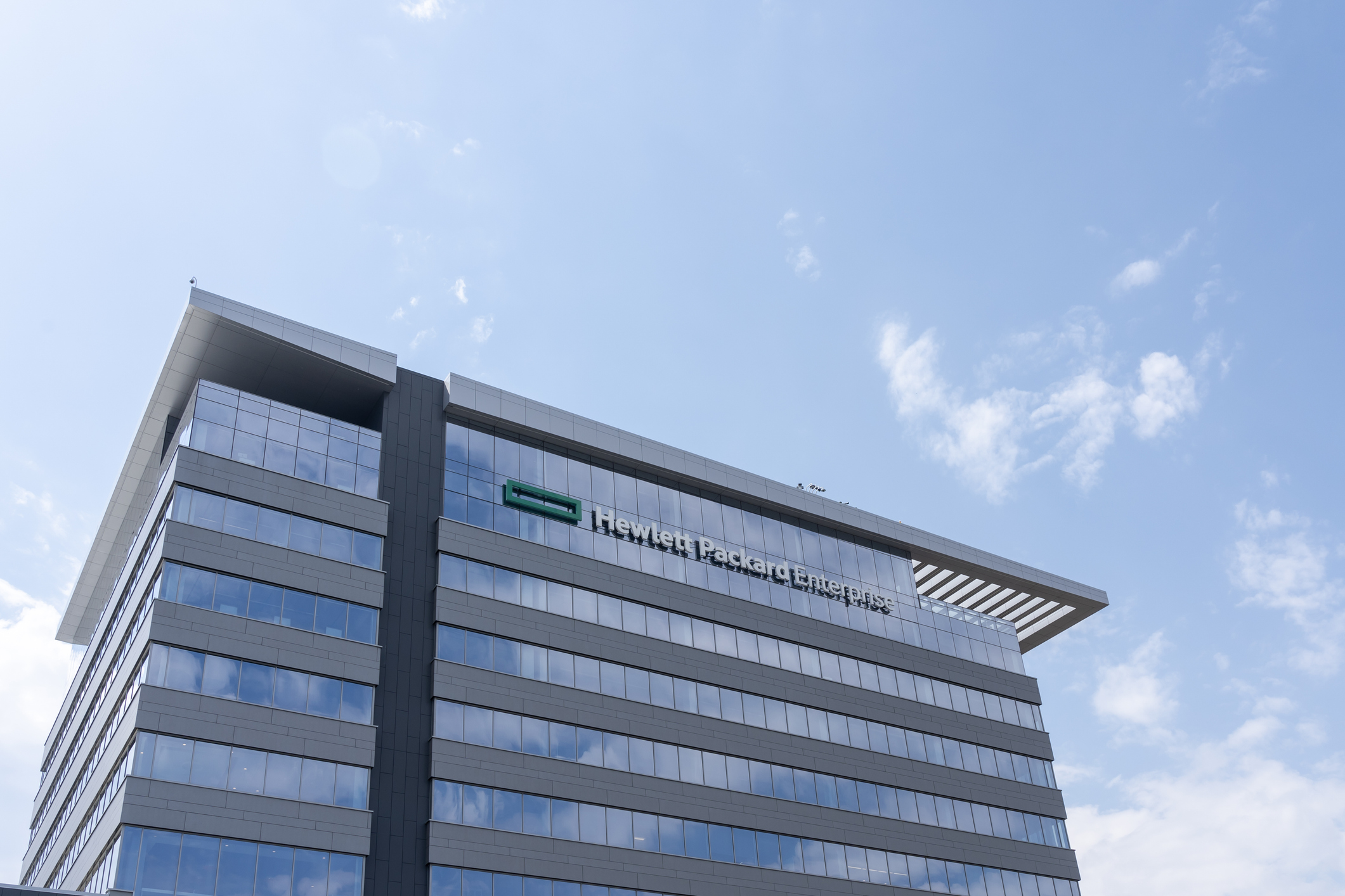 Modern glass and steel office building with company signage on facade under blue sky