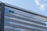 Modern glass and steel office building with company signage on facade under blue sky