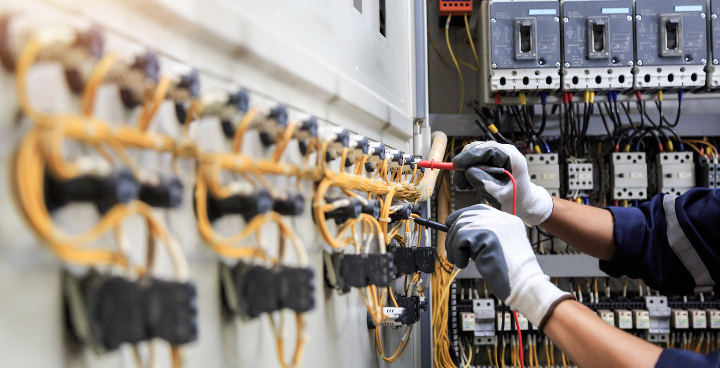 Electrician installing yellow wiring in industrial circuit breaker panel with safety gloves