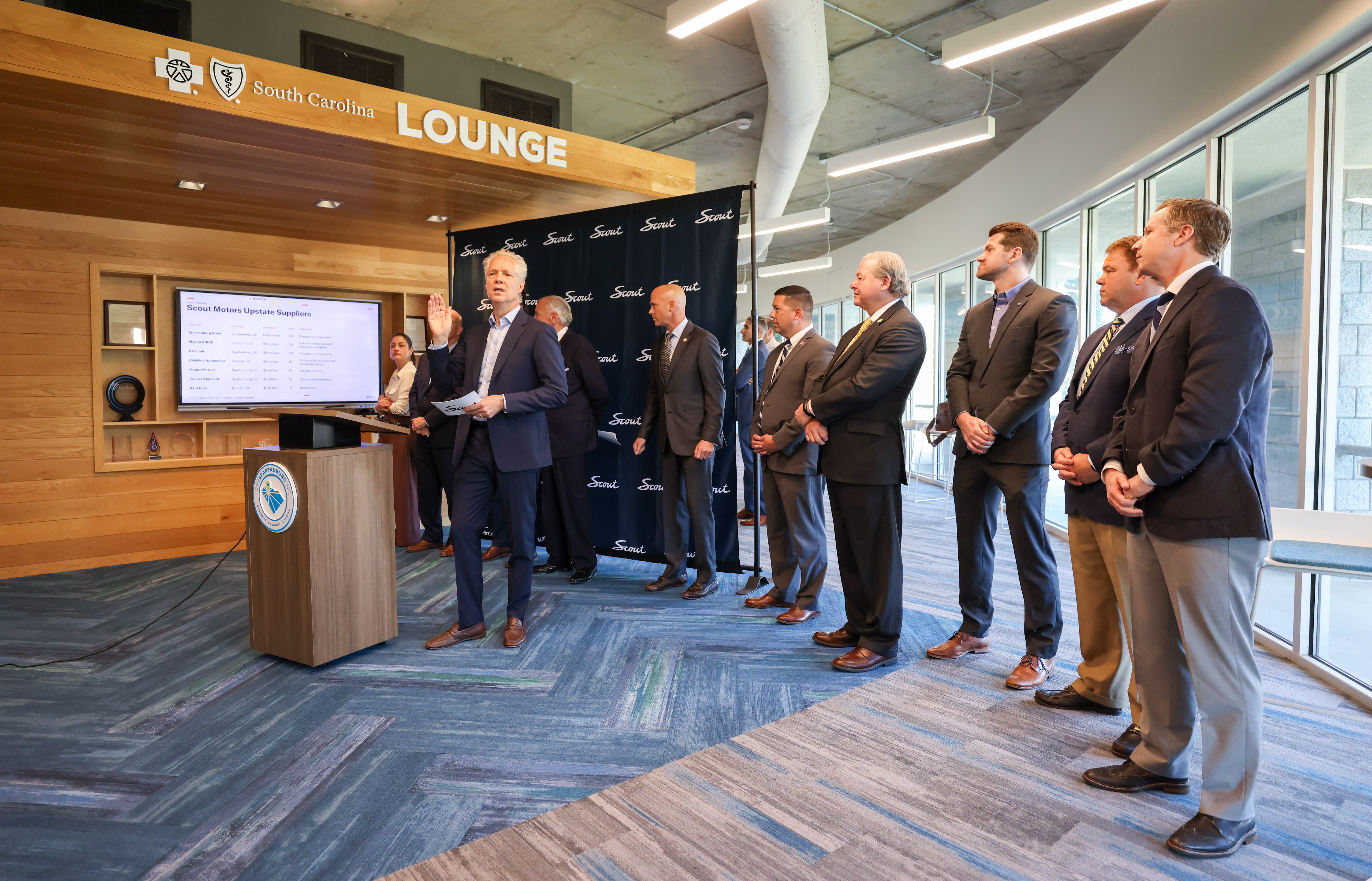 Business professionals gathered in South Carolina Lounge for corporate presentation at podium with display screen
