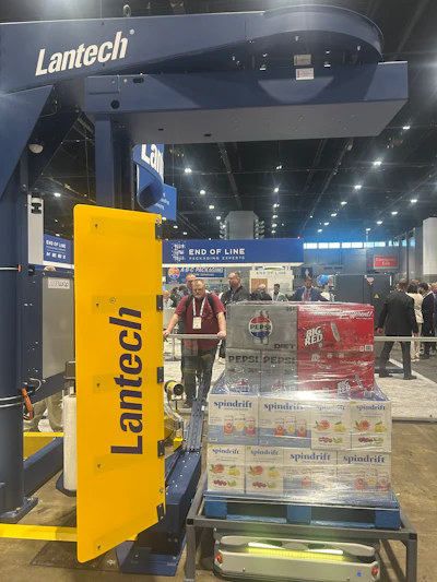 Lantech stretch wrapping machine displayed at trade show with packaged products and attendees in background