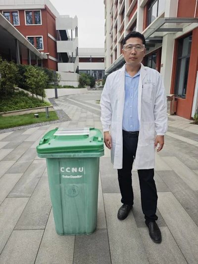 Man in white lab coat standing beside green CCNU waste bin on university campus courtyard