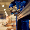 Industrial worker in blue uniform using angle grinder on metal with sparks flying in factory setting