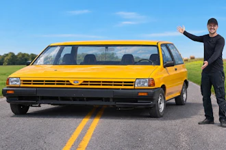 Man in black clothing posing beside a bright yellow vintage minivan on a rural highway with green fields and blue sky