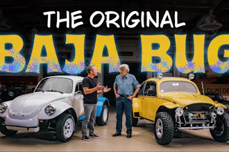 Two men stand between a white and yellow modified Baja Bug vehicles in a garage workshop setting.