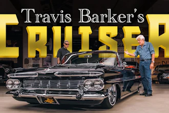 Travis Barker's classic black convertible cruiser displayed in showroom with two men standing beside the vintage 1950s car