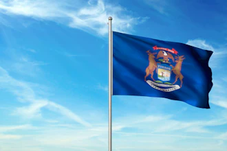 Michigan state flag waving on a flagpole against a blue sky with white clouds