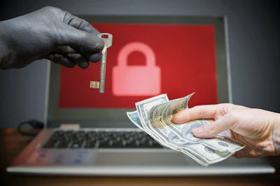 Ransomware extortion concept: hands exchanging money and key with padlock symbol on laptop screen