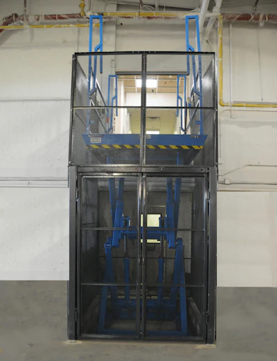 Industrial personnel lift cage with blue frame and safety railings in warehouse facility