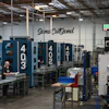 Industrial manufacturing facility with blue CNC machines and Sena CutSend signage on warehouse wall