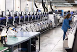 Industrial warehouse facility with rows of automated sorting machines and a worker in blue uniform monitoring operations