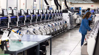 Industrial warehouse facility with rows of automated sorting machines and a worker in blue uniform monitoring operations
