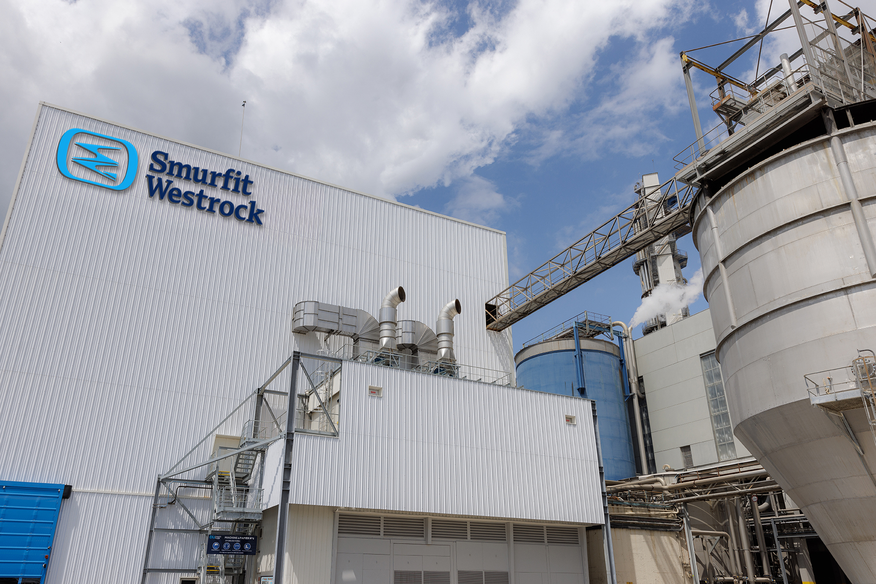 Smurfit Westrock industrial manufacturing facility with blue logo on corrugated metal building and storage tanks