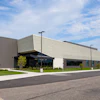 Modern industrial building with metal siding, glass entrance, and manicured landscaping under blue sky