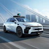 White autonomous taxi vehicle with blue accents driving on elevated highway with city skyline in background