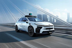 White autonomous taxi vehicle with blue accents driving on elevated highway with city skyline in background