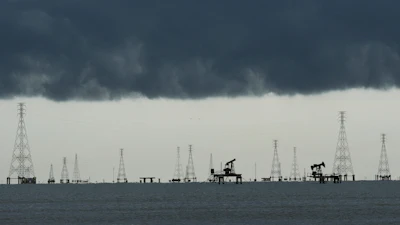 Offshore oil and gas extraction platform with multiple derricks and pump jacks silhouetted against dark storm clouds