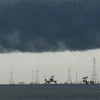 Offshore oil and gas extraction platform with multiple derricks and pump jacks silhouetted against dark storm clouds