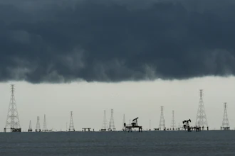 Offshore oil and gas extraction platform with multiple derricks and pump jacks silhouetted against dark storm clouds