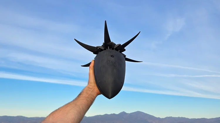 Person holding black spiked helmet against blue sky with mountains in background