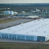 Aerial view of large industrial warehouse facility with white roof and blue walls in rural landscape